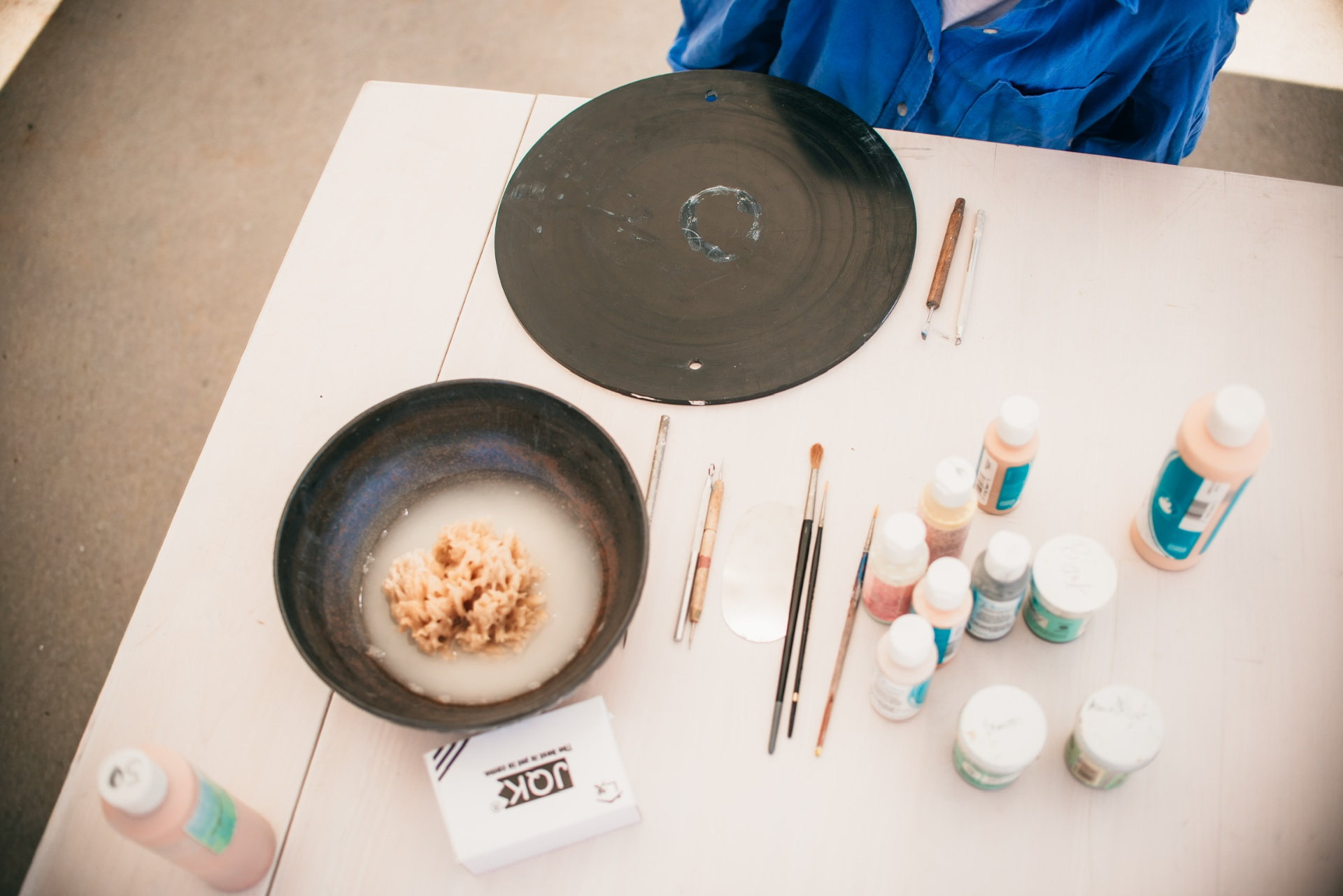 Overhead view of a clay bat, sponge bowl, tools and glazes on the worktable