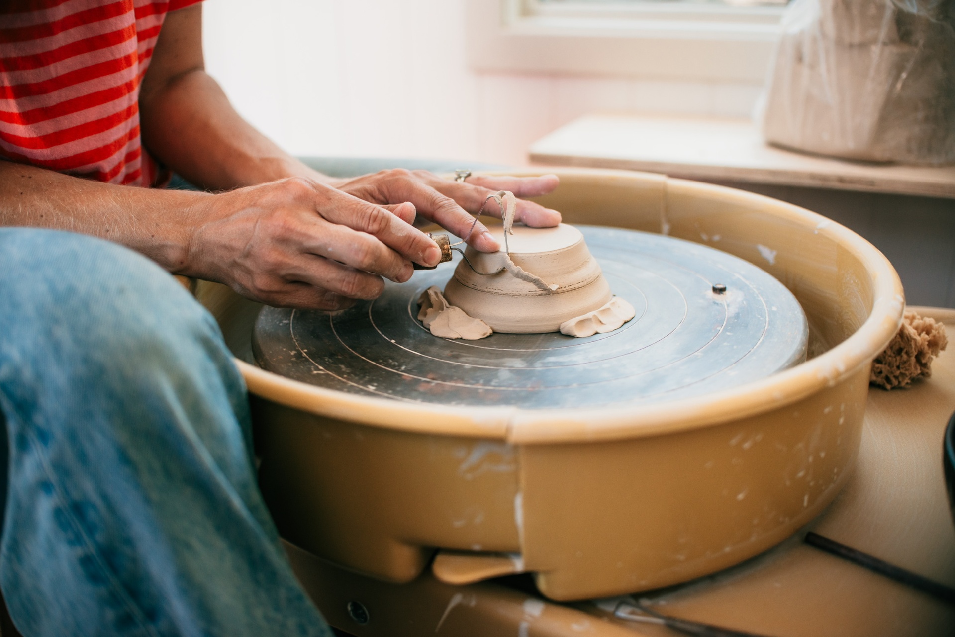 Hands trimming the foot of a freshly thrown bowl on the wheel